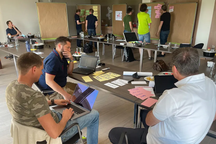 Teilnehmende arbeiten in Gruppen mit Laptops, Kärtchen und Pinnwänden