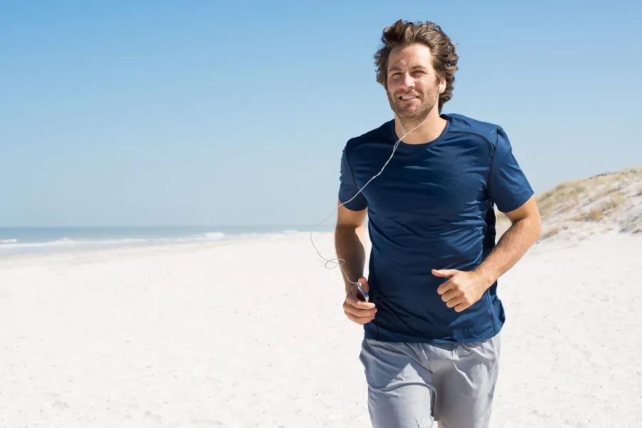Glücklicher Mann joggt mit Kopfhörern am Strand