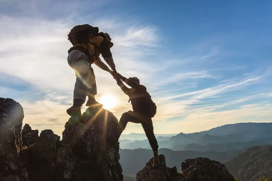 Zwei Wanderer helfen sich gegenseitig auf einen Berggipfel